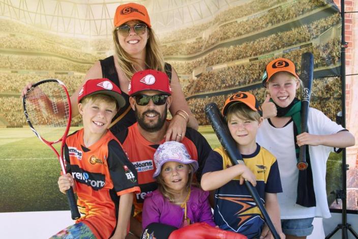 "A Mum and Dad are surrounded by their four children. Everyone is wearing sporting gear with tennis rackets."